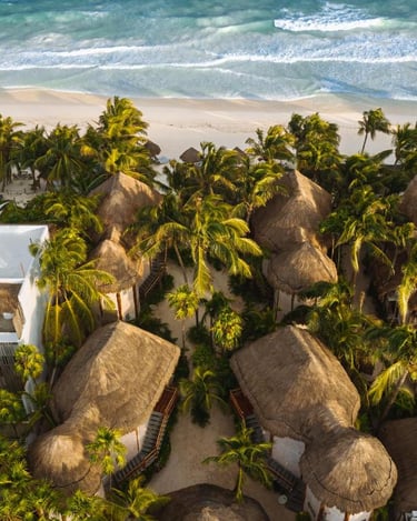 Aerial view of luxury thatched roof bungalows and palm trees on a white sand beach in Tulum, Mexico.