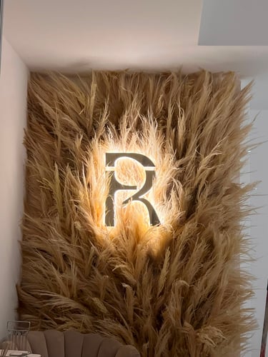 "Decoração de parede comercial com texturas de pampas e flores secas com logótipo iluminado por Char