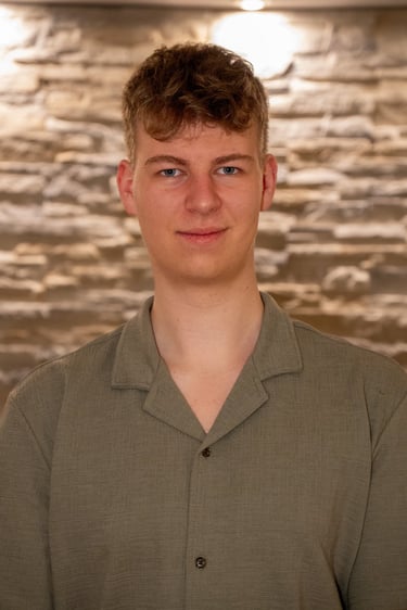 Porträt eines jungen Mannes mit blonden Haaren in einem grünen Hemd vor einer Steinmauer.