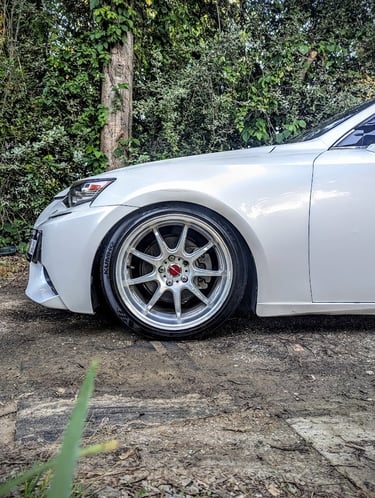 White luxury sedan featuring aftermarket chrome alloy wheels and lowered suspension parked on dirt.