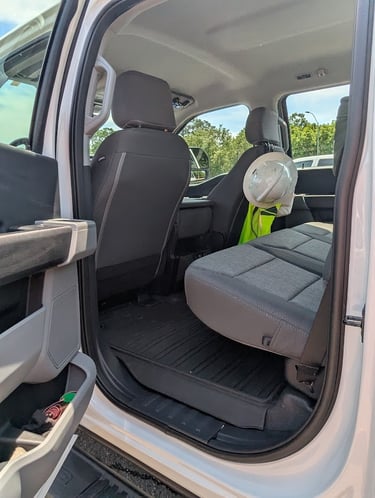 Interior view of a white pickup truck back seat with a hard hat and safety vest for construction work.