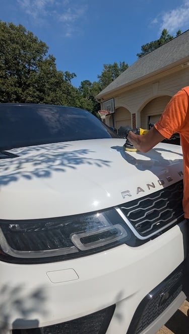 A detailer uses a dual action polisher to buff the hood of a white Range Rover for paint correction.