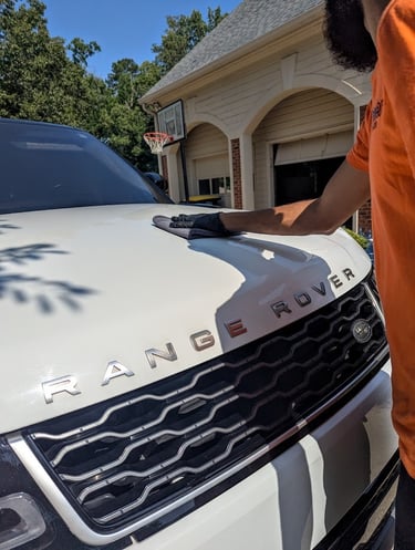 Professional car detailer wiping a white Range Rover hood with a microfiber cloth for mobile detailing.