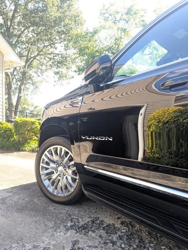 A black GMC Yukon SUV parked on a driveway, highlighting the polished exterior and chrome wheels.