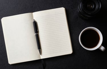 Top-down view of a designer's desk in a Spanish studio. A minimalist notebook with clean handwritten notes, a sleek black pen, and a cup of black coffee. Organized and professional aesthetic.