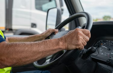 A detailed close-up of a logistics professional's hand firmly gripping a steering wheel of a modern truck in North American / US. Professional attire visible.