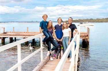 Family of five pose on a jetty in Mosman Bay for portrait by Fisher Photography
