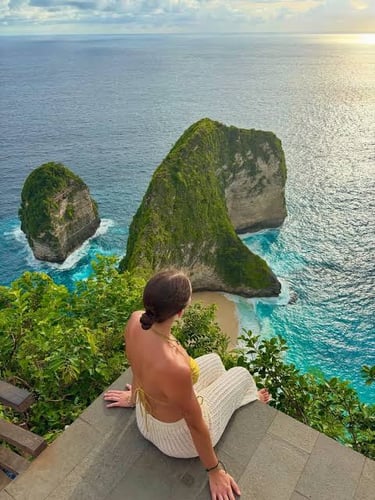 A woman looks over Kelingking Beach in Nusa Penida, Bali, featuring the iconic T-Rex shaped cliff.