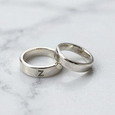 Close-up of a handcrafted silver ring with a subtle jade green accent, resting on a smooth gray stone.