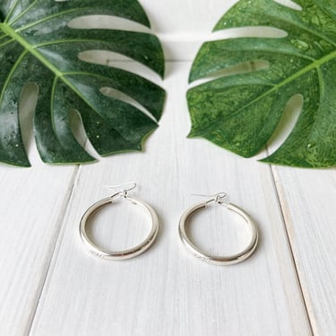 Delicate silver earrings with jade green details, photographed against a muted green background.