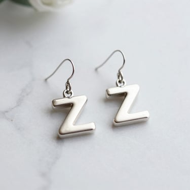 Delicate silver earrings with jade green details, photographed against a muted green background.