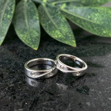 Close-up of a handcrafted silver ring with a subtle jade green accent, resting on a smooth gray stone.