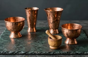 Polished copper ritual vessels and a small wooden mortar on a dark slate green table, reflecting a warm, tranquil glow.