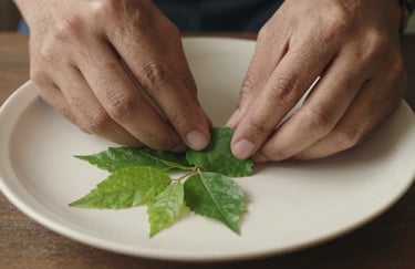 A close-up of a person's hands delicately arranging fresh neem and tulsi leaves on a warm off-white ceramic plate.