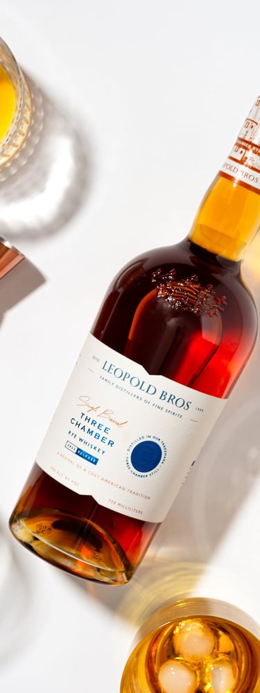 a bottle of Leopold Bros Three Chamber Rye surrounded by glasses of whiskey