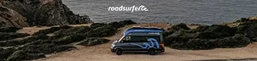 A Roadsurfer camper van parked on a rugged cliff overlooking the ocean at sunset.