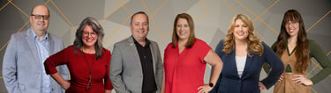 Professional business team portrait featuring diverse corporate staff smiling against a geometric background.