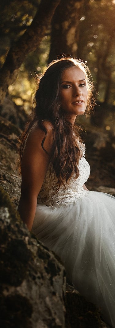 Ritratto di una sposa in un bosco in montagna, illuminata dai raggi del sole filtrati dai rami degli alberi