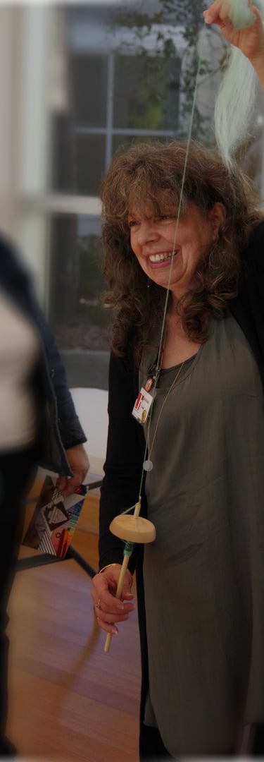 Photo of Linda Nickel demonstrating spinning yarn with a drop spindle.