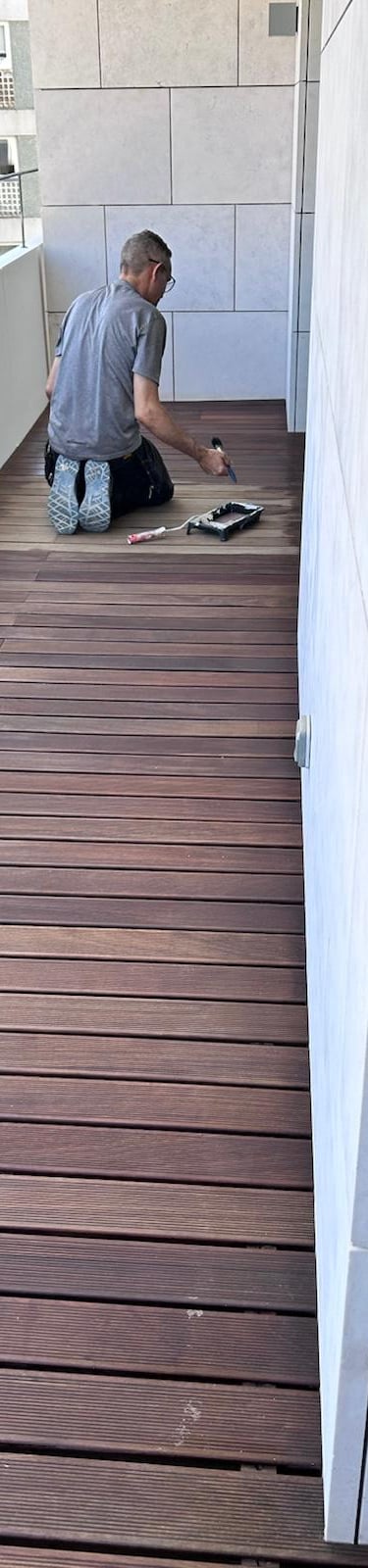 Professional contractor applying wood stain to a modern apartment balcony deck.