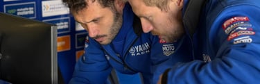 two men in blue jackets looking at data on a laptop