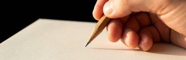 Main qui tient un crayon de papier au-dessus d'une feuille blanche