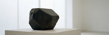 Forme géométrique en pierre noire sur socle blanc dans un espace d'exposition blanc