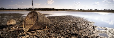 Fine art panorama of traditional woven fishing baskets on cracked riverbank soil beside still water in Zimbabwe.