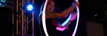 A performer with red hair spins a glowing LED hula hoop during a night stage show. 