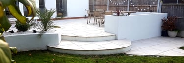 Modern chic raised porcelain patio with white rendered walls and planters