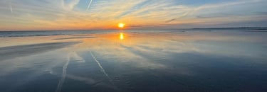 a sunset on a beach with a plane flying over the water