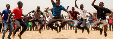 Young dancers mid-jump during an energetic street dance battle in Nguekhokh, dusty ground, bright natural light, action framing.