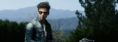 a man in a denim jean jacket and sunglasses sitting on a motorcycle in the mountains