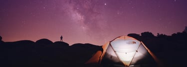 a person standing in front of a tent with a bright purple starry night sky