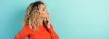A curly-haired woman putting a finger to her chin, deep in thought