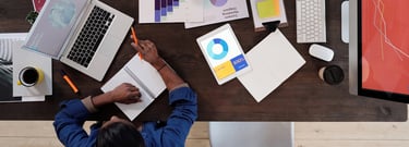 A woman works at her desk, surrounded by papers and devices displaying marketing metrics