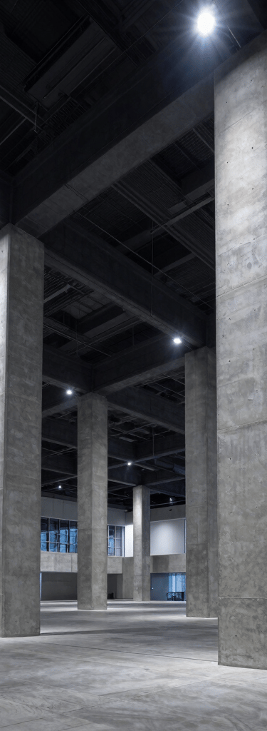 Wide-angle architectural environmental shot of a massive modern convention center interior, sharp concrete columns, dramatic cool-toned spotlighting, crisp industrial composition