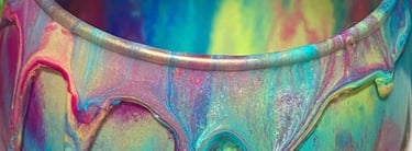 A glass used for a multi color acrylic paint pour shows a vibrant rainbow dripping from the rim
