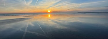 a sunset on a beach with a plane flying over the water