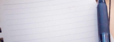 A compass on top of a notebook, with a pen and camera on the side