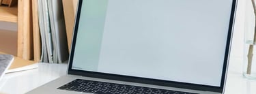 Laptop on a white desk, with houseplants and notebooks around