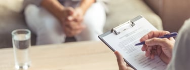 Zwei Personen in einer Psychotherapiesitzun. Der Psychotherapeut macht sich Notizen.