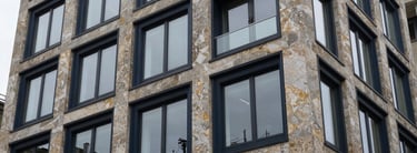 Close-up of a modern, high-end residential building facade in Zürich, elegant stone and glass, soft overcast daylight, deep navy and gold tones, 35mm lens