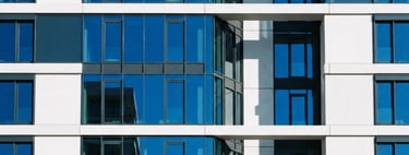 Bright, high-contrast architectural facade with clean geometric lines, cobalt blue reflections in glass, sharp daylight shadows, minimalist composition, 35mm lens.