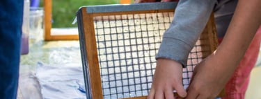 The hands of two children lifting a small screen while making paper.