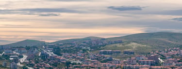 Panoramic aerial view of a Turkish city nestled in rolling hills under a cloudy sunset sky.