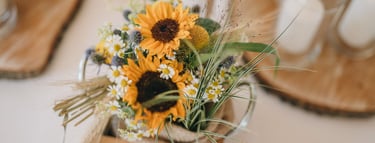 Rustikales Tischgesteck für eine Hochzeit mit leuchtenden Sonnenblumen und Gänseblümchen