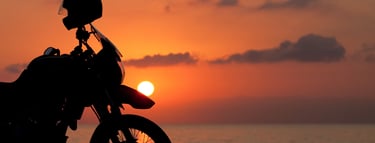 a motorcycle parked on a rocky beach at sunset