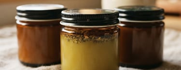 Macro close-up of amber glass jars of herbal balm resting on textured raw linen, soft morning window light, warm earth tones, shallow depth of field, 35mm