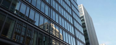 Photography of a sleek, contemporary commercial glass building in the City of London, reflecting a bright blue sky, conveying professional growth and urban success.